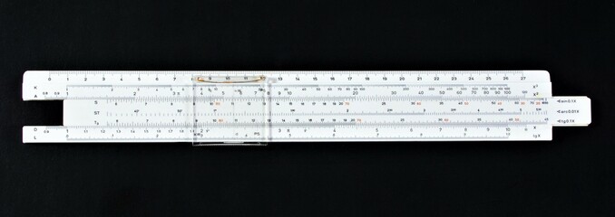A slide rule isolated on a black background. An analog computing device with a scale for...