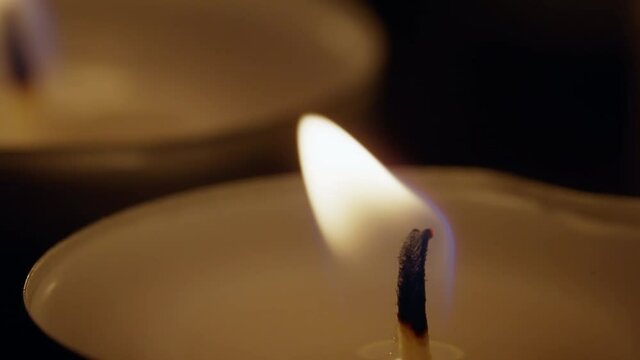 Close up burning tea lights isolated on black background moving in wind shot in 4k super slow motion