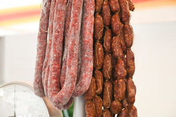 There are two types of meat sausages hanging next to the scales