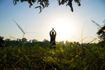 silhouette of a boy doing surya namaskar in park near sun and river - health concept