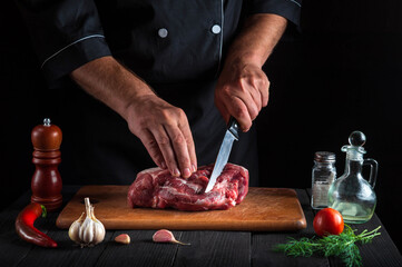 Cook cuts meat with a knife in the kitchen prepares food. Vegetables and spices on the kitchen table in a restaurant to prepare a delicious lunch