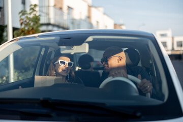 Multiracial couple riding together in car. Young european woman holding parcels delivering home....
