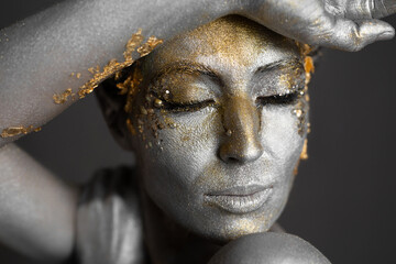 Portrait of a beautiful female model with gold and silver paint on her skin and hair in the studio.