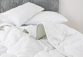 Fototapeta na wymiar White pillows in cotton pillowcases lie on a rumpled bed. An airy white satin blanket lies casually on the bed. White new bedding