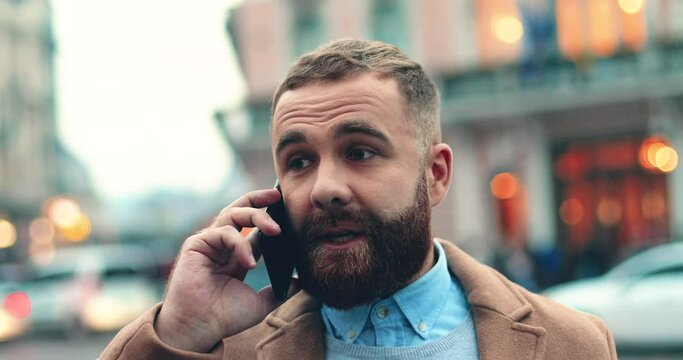Close up of caucasian businessman with beard standing on street and solving problems on mobile phone with serious facial expression.