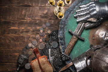 Knight sword, shield and armor in the light of the burning candle on the wooden flat lay background...