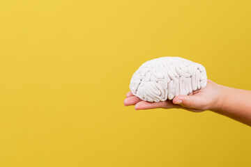 panorámica de las manos de una persona con un cerebro en sus manos en fondo amarillo - obrazy, fototapety, plakaty