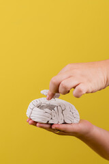 vertical de las manos de una mujer reparando un cerebro en fondo amarillo
