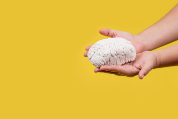 Manos de una persona con un cerebro en sus manos en fondo amarillo - obrazy, fototapety, plakaty