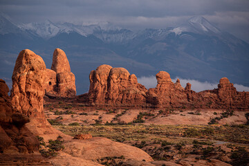 Sunset light illuminates the rocky terrain of Arches National Park with the snowcapped La Sal Mountains in the background, Utah