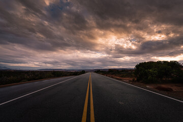 Long desolate desert road in the middle of nowhere under dramatic stormy sunrise sky