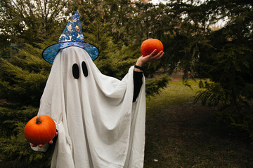 Ghost holding pumpkins outside in the park. Halloween and autumn concept.