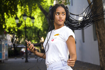 young woman with loose braids cell phone in hands and wearing headphones
