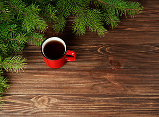 Christmas background fir branches with a red cup of coffee on a wooden background.