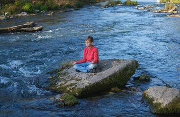 teenage boy meditates on a rock among the waves of a seething river