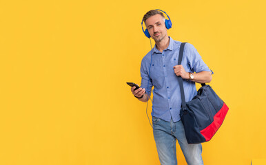 mature man listening music on phone hold sports bag on yellow background, copy space, message.