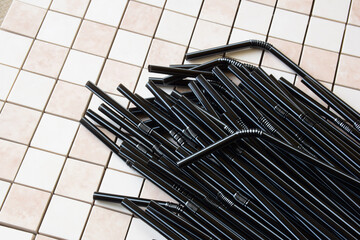 Several dozen black cocktail tubes on the background of square ceramic tiles. On the left there is...