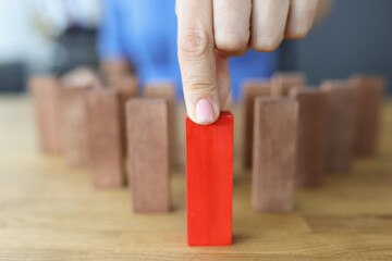 Female hand selects red wooden block among brown ones