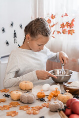 Cute little girl whips ginger dough to make cookies for halloween in the home kitchen. Treats and preparations for the halloween celebration