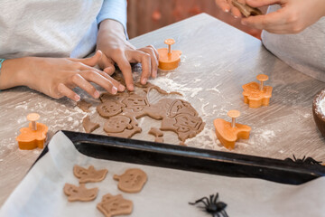 Preparing to celebrate halloween and preparing a treat. Children cut out baking pans for Halloween cookies and a baking sheet of raw cookies on the table. Lifestyle