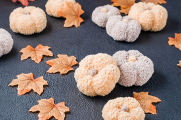 Handcraft autumn still life - knitted pumpkins and maple fabric leaves on a black background. Halloween and Thanksgiving decor. Copy space