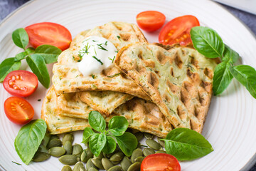 Appetizing zucchini waffles, tomatoes, pumpkin seeds and basil on a plate on the table. Vegetable diet vegetarian food. Close-up