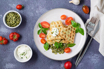 Ready-to-eat delicious zucchini waffles, tomatoes, basil and pumpkin seeds on a plate on the table. Vegetable diet food. Top view