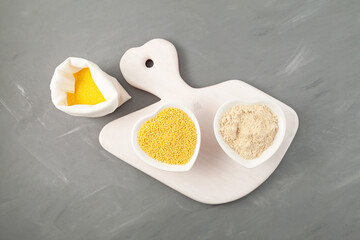 Hulled millet and coarse flour on white cutting board, top view. Yellow grain, grey background, copy space