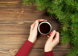 Christmas background fir branches hands hold a red cup of scofe on a wooden background.