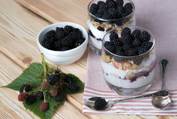 Fototapeta na wymiar Blackberry berries in a summer dessert - cheesecake in glasses on a wooden background. Healthy snack