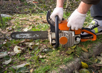 a man's hands start a chainsaw in the garden