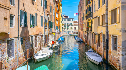 Fototapeta na wymiar Lovely Venetian nook on sunny summer day. Narrow water canal with boats and residential houses along. Venice, Italy