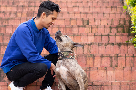 Man looking at his pet and smiling while petting it. Tender dog and its owner. Man dressed in a blue buso bending down to touch his pet on a narnaja background.