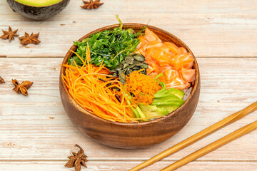Norwegian salmon poke bowl with white rice, grated carrot, wakame seaweed salad, pumpkin seeds, ripe avocado, star anise, wooden chopsticks and masago roe