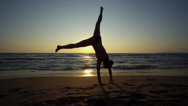 Teenager female silhouette doing cartwheels at beach sunset