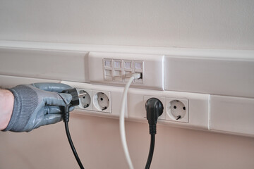 Connection to the electrical network in the office, a gloved hand holds the cord to connect to the...
