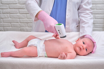 Doctor checks the temperature of the newborn baby with a thermometer. A nurse in uniform measures the child fever with a thermometer