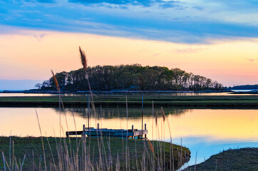 Tidal marsh at sunset, Niantic Connecticut with view of dock and Watts Island at sunset, blue hour. Golden hour sky with trees and island in silhouette. 