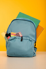Bright backpack and school stationery on table, vertical image
