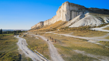 A group of riders on horseback moves along the canyon along the white rocky mountain. Shooting from a drone. Copy space.