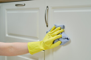 Woman hand wipes the front of the cabinet with a rag while cleaning the home kitchen