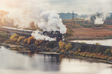 Fototapeta na wymiar Retro steam train moves along the lake at autumn sunrise.