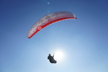 A paraglider flies a glider against a blue sky in good sunny weather. Close up