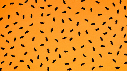 Many black paper bats on a bright orange background, seamless drawing, pattern.Concept for a holiday card, Halloween banner, top view, flat lay.Festive decor.