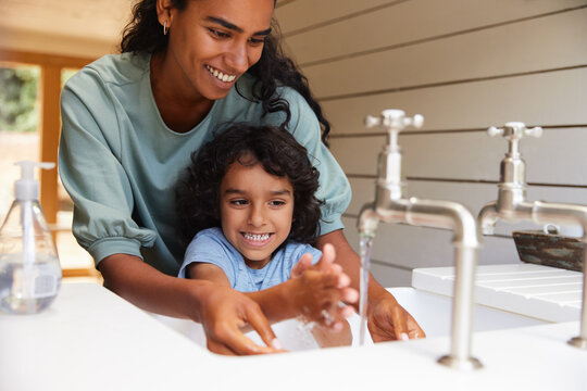 Mother Helping Young Son Wash Hands In Sink