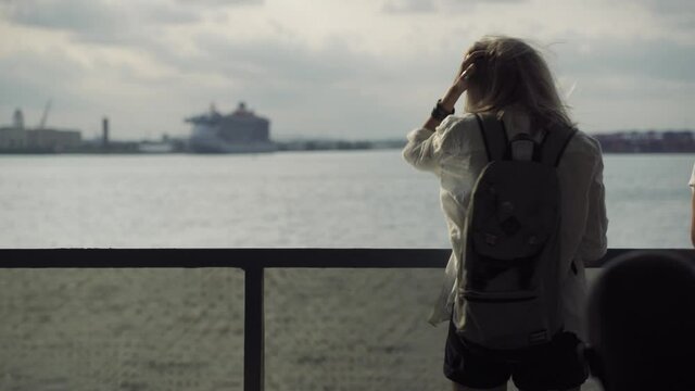 A young teenage girl takes in the view of lower Manhattan from a ferry. Blond woman watching liberty statue on background from the pier in the harbor. Travel, adventure, tourism concept.