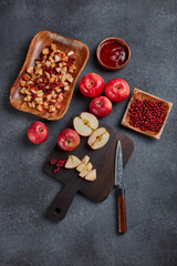 Still life with fresh lingonberries, red appples with knife on black cutting board and homemade jam on dark background. Top view