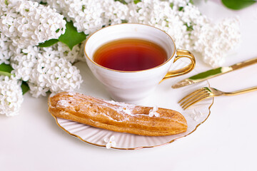 Tasty eclair on plate with fork and cup of tea, with flower bouquet