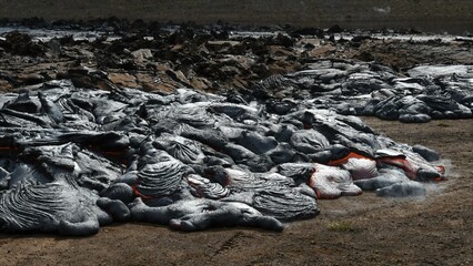 Pahoehoe lava flow at Fagradalsfjall, Iceland. Lava crust is gray and black, molten lava is red and orange. Steam and gas are visible.