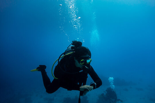Woman scuba diver swimming in deep blue checking her dive computer